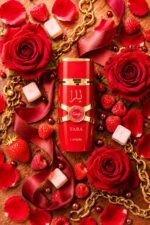 Vue de dessus du flacon Lattafa Yara Candy rouge et or couché parmi des roses rouges épanouies, framboises, fraises, guimauves blanches, ruban bordeaux satiné, chaîne dorée et perles rubis sur fond bois acajou