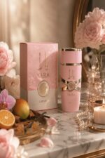 Flacon et boîte du parfum Lattafa Yara rose et or posés sur un marbre, entourés de pivoines roses, mangue, orange, cannelle, vanille et perles dans une ambiance dorée